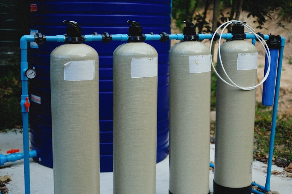 Services Four beige tanks in an outdoor water treatment setup with blue piping.