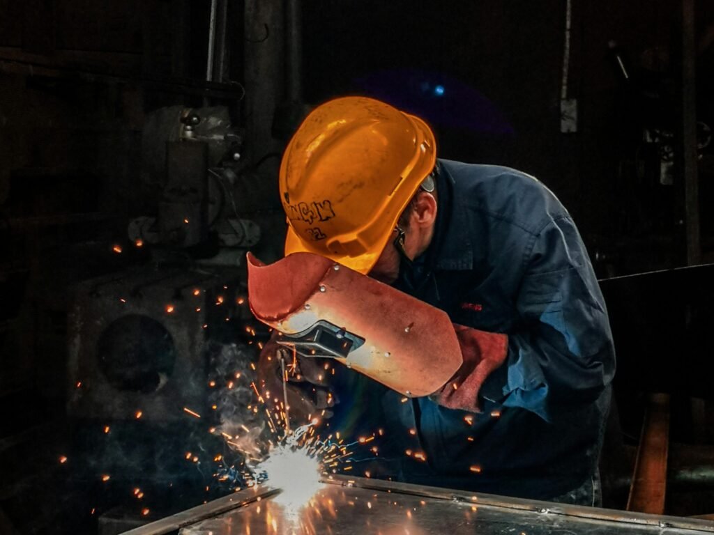 Services A welder wearing protective gear works on metal in an industrial workshop, surrounded by sparks.