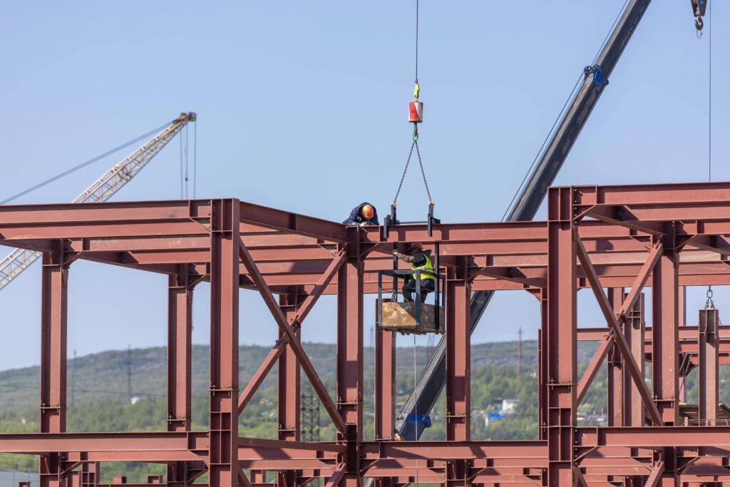 Services Construction workers assembling steel frame structure with cranes in daylight outdoors.